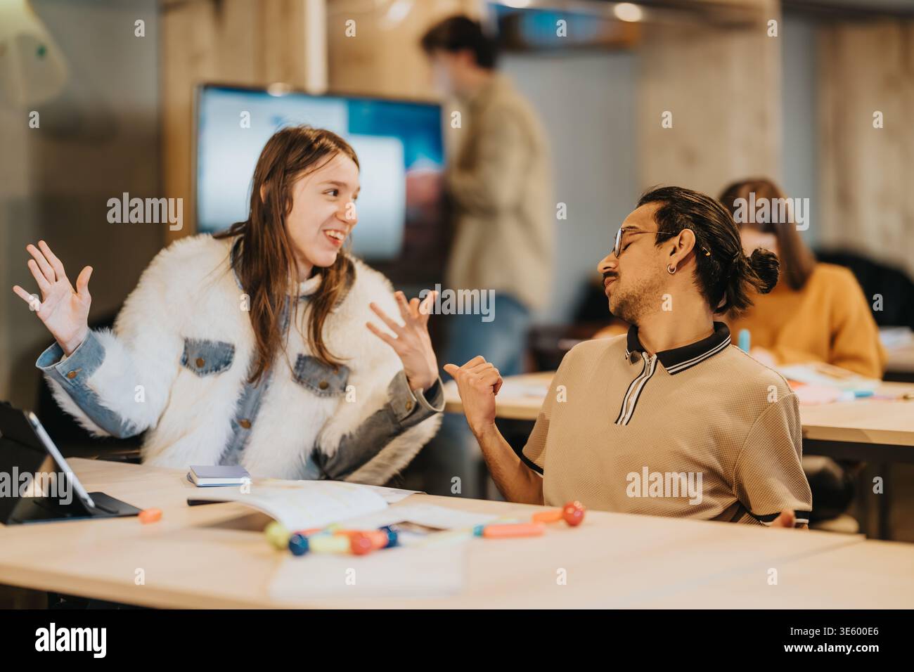 Two students having an animated discussion during a collaborative study session in a modern workspace Stock Photo