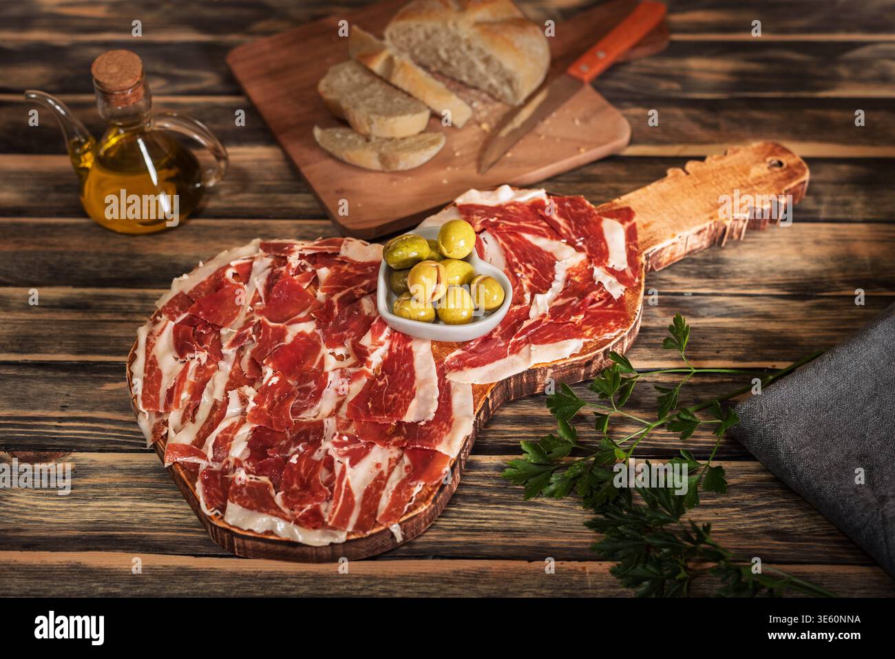 Guitar-shaped board with Serrano ham with bread, olive oil and olives Stock Photo