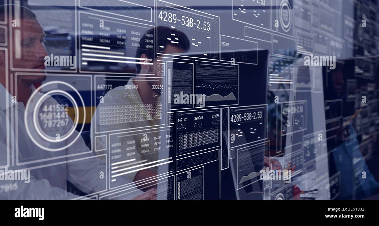 Working IT team analyzing code on monitors at adjacent desks in office, wearing shirts with HUD Stock Photo