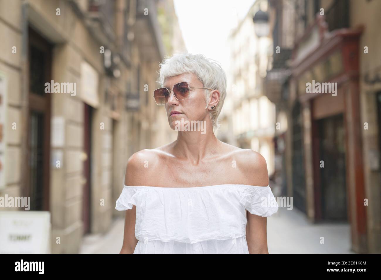 A woman wearing a white dress and sunglasses stands in front of a ...