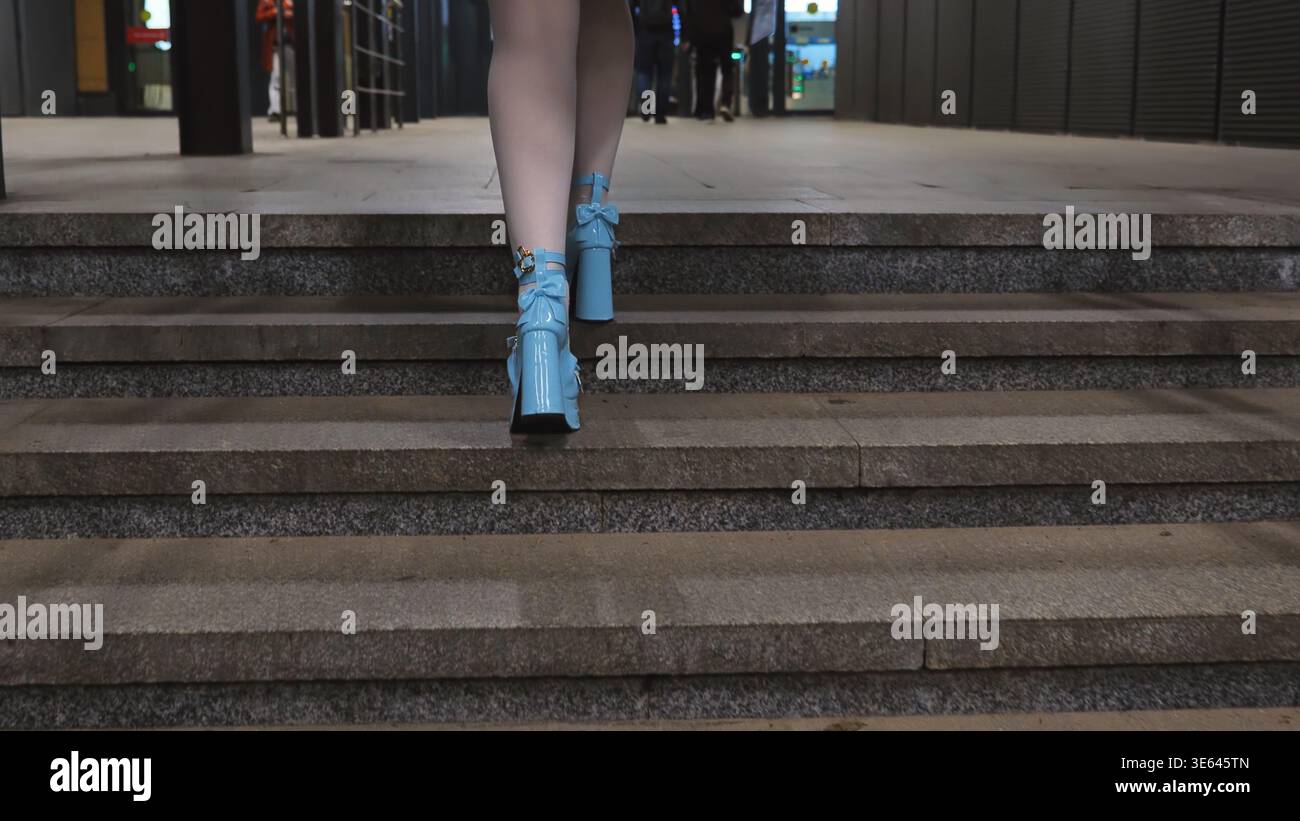 Woman walking up stairs wearing blue glossy platform heels with decorative bows Stock Photo