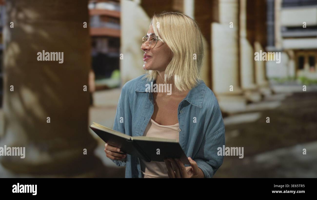 Woman holding a book with both hands, reading aloud near classical columns at a building; serenity quiet study. Stock Photo