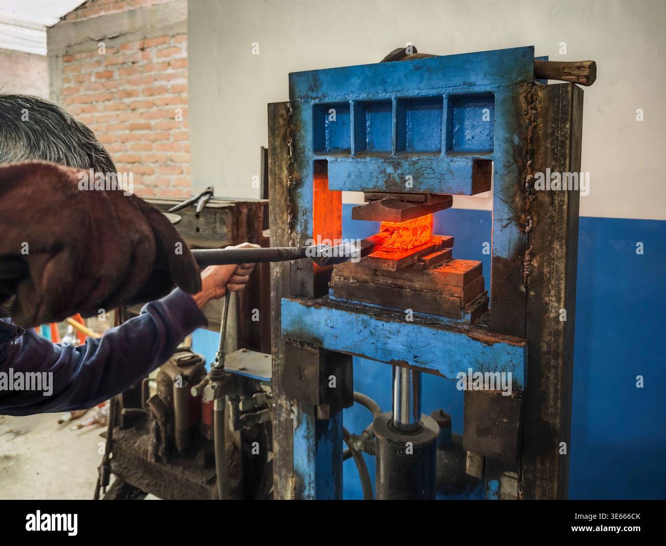 Professional blacksmith forging damascus steel using a powerful hydraulic press in a workshop. Stock Photo