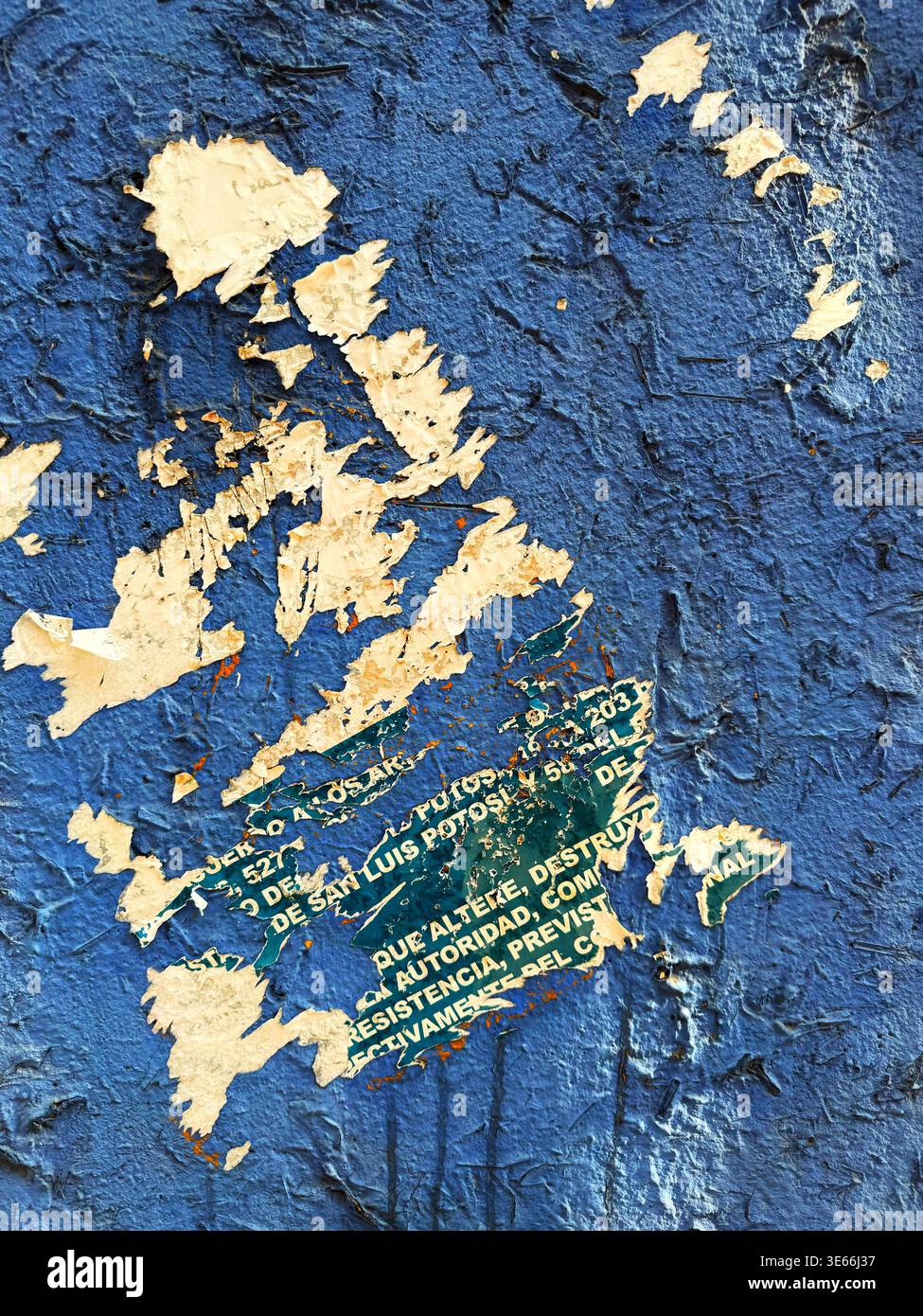 Close up view of a rough blue painted wall with torn paper posters revealing layered textures Stock Photo
