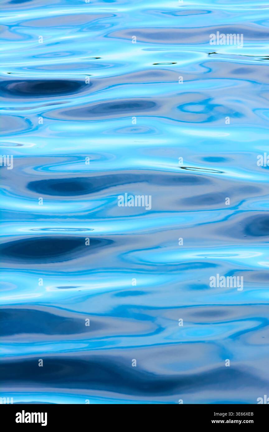 Vertical image of fluid light patterns on rippling water reflecting the sky and clouds in colours of blue and grey. Stock Photo