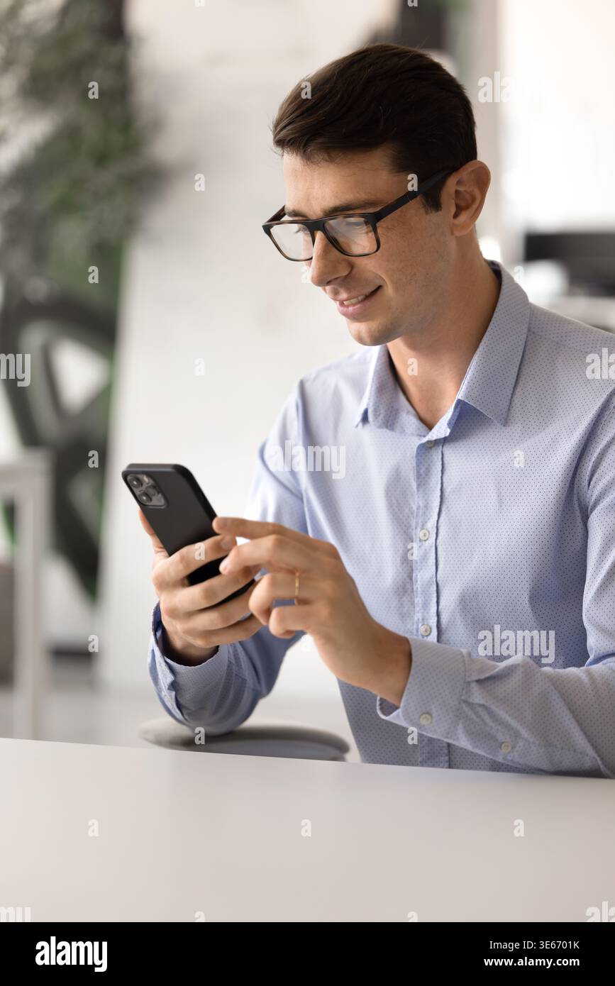 Young Spaniard man in casual shirt using smartphone at workplace Stock Photo