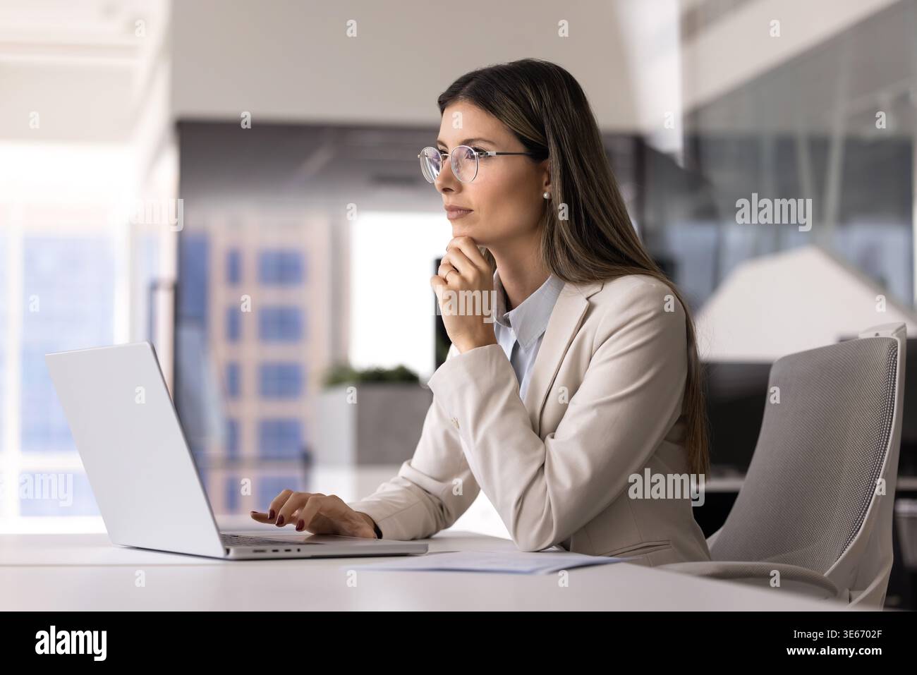 Woman thinking while working at laptop in office Stock Photo