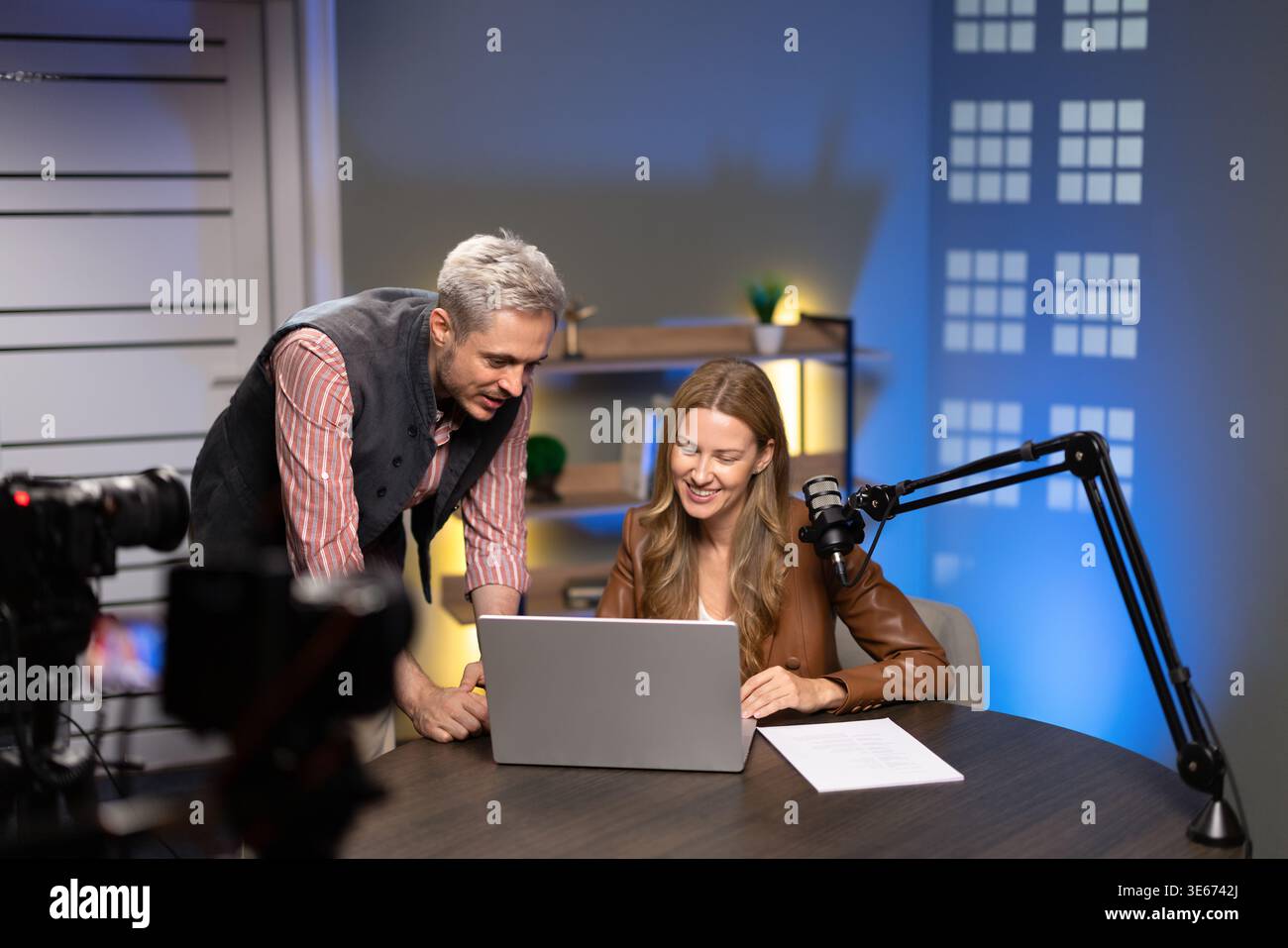 Hosts collaborating on digital content, using microphone and laptop Stock Photo