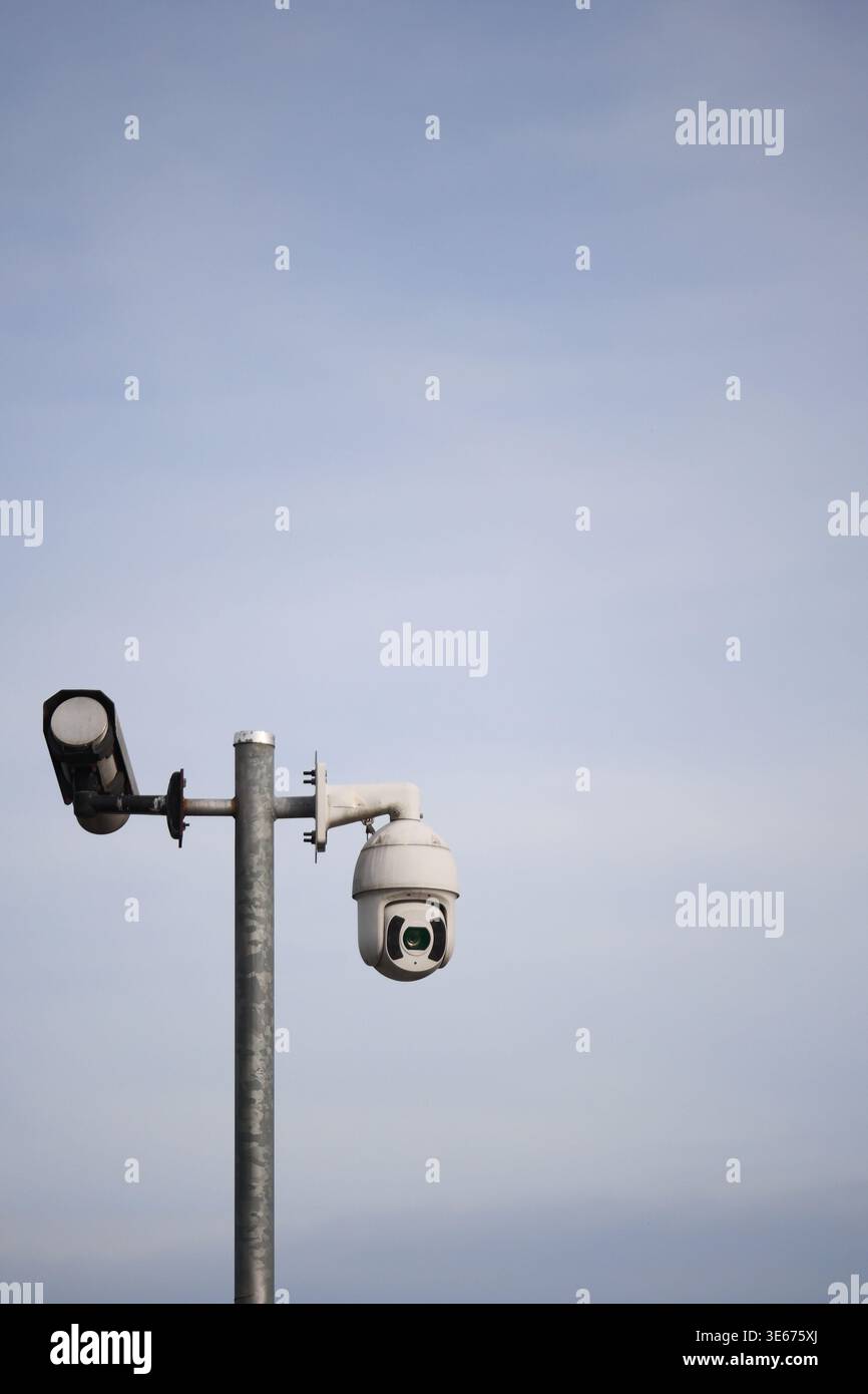 Security camera on a pole with a light fixture nearby Stock Photo