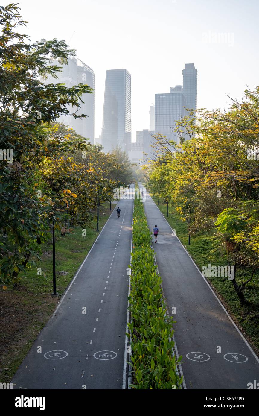 Bangkok Thailand January 16 2026. Single jogger runs along paved road in Benchakitti Park with trees and skyline in distance. Stock Photo