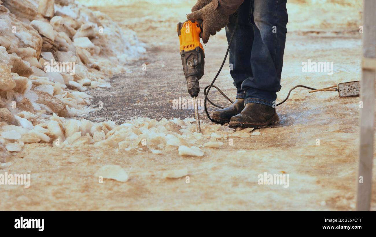 Worker using jackhammer to remove ice from a snow-covered sidewalk during winter Stock Photo