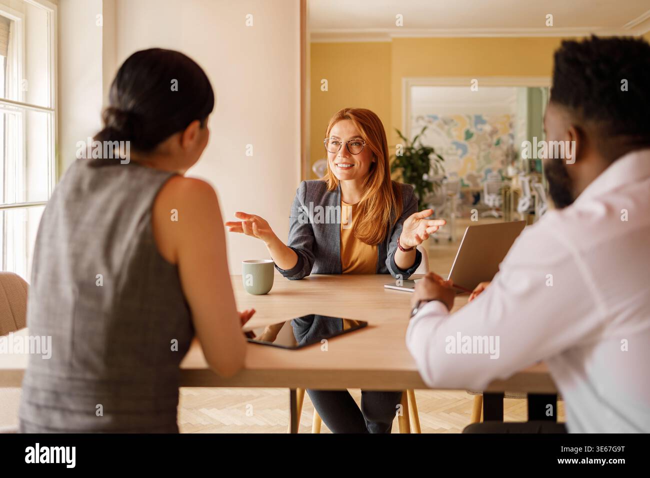 Confident businesswoman in eyeglasses discussing project plans with colleagues during collaborative meeting Stock Photo