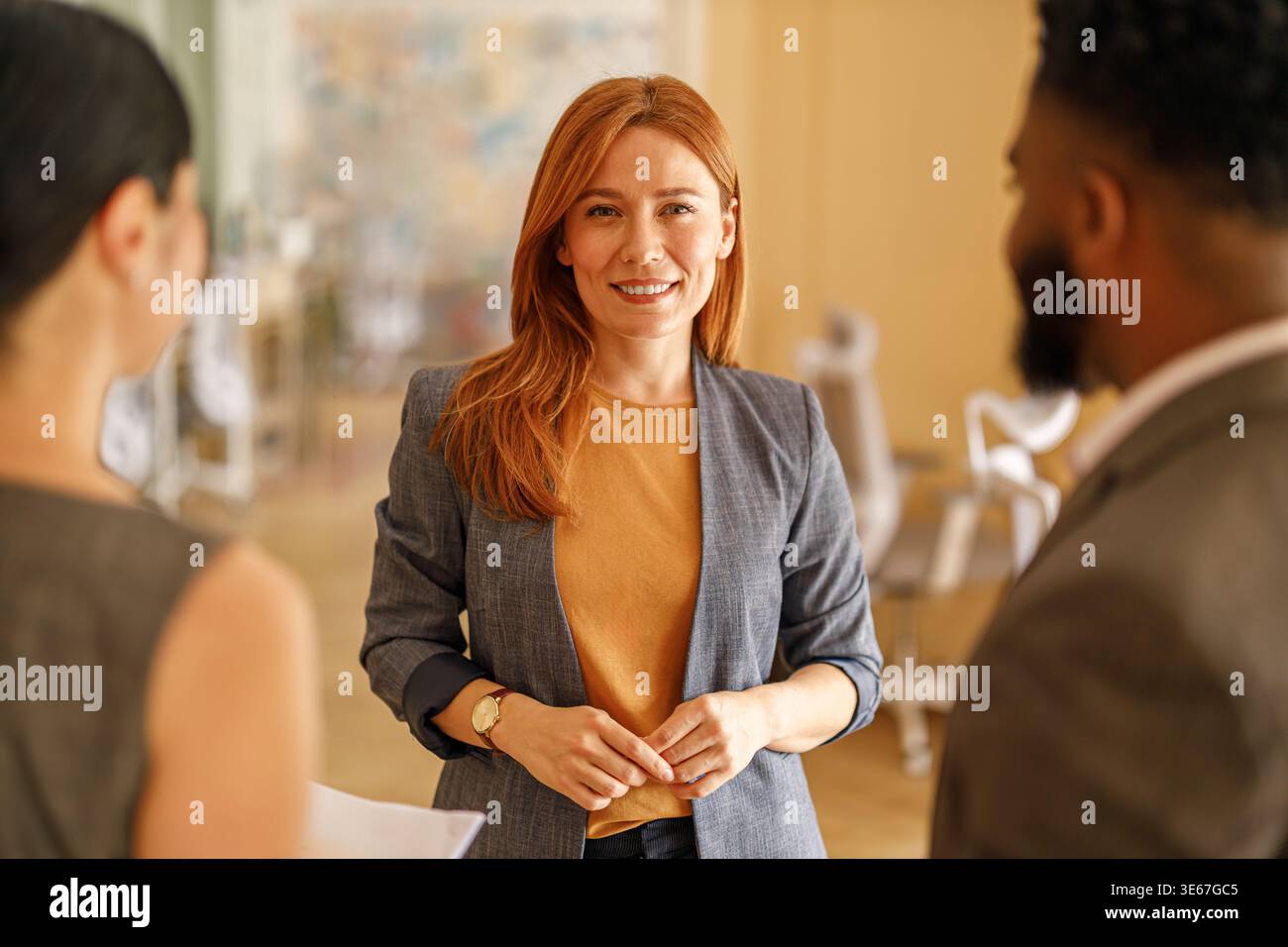 Confident female manager smiling at camera while discussing ideas with professional colleagues in modern office Stock Photo