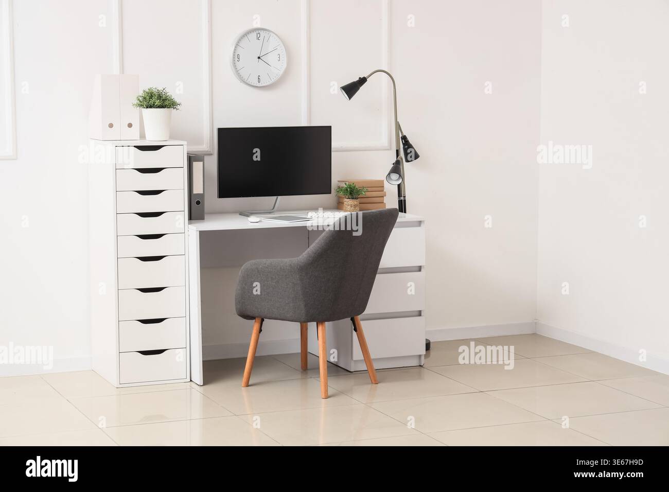 Workplace with computer, lamp and clock on light wall in office Stock Photo