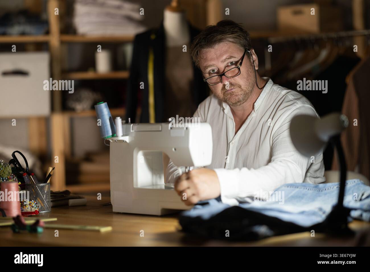 Middle-aged male dressmaker working with sewing-machine at night Stock Photo