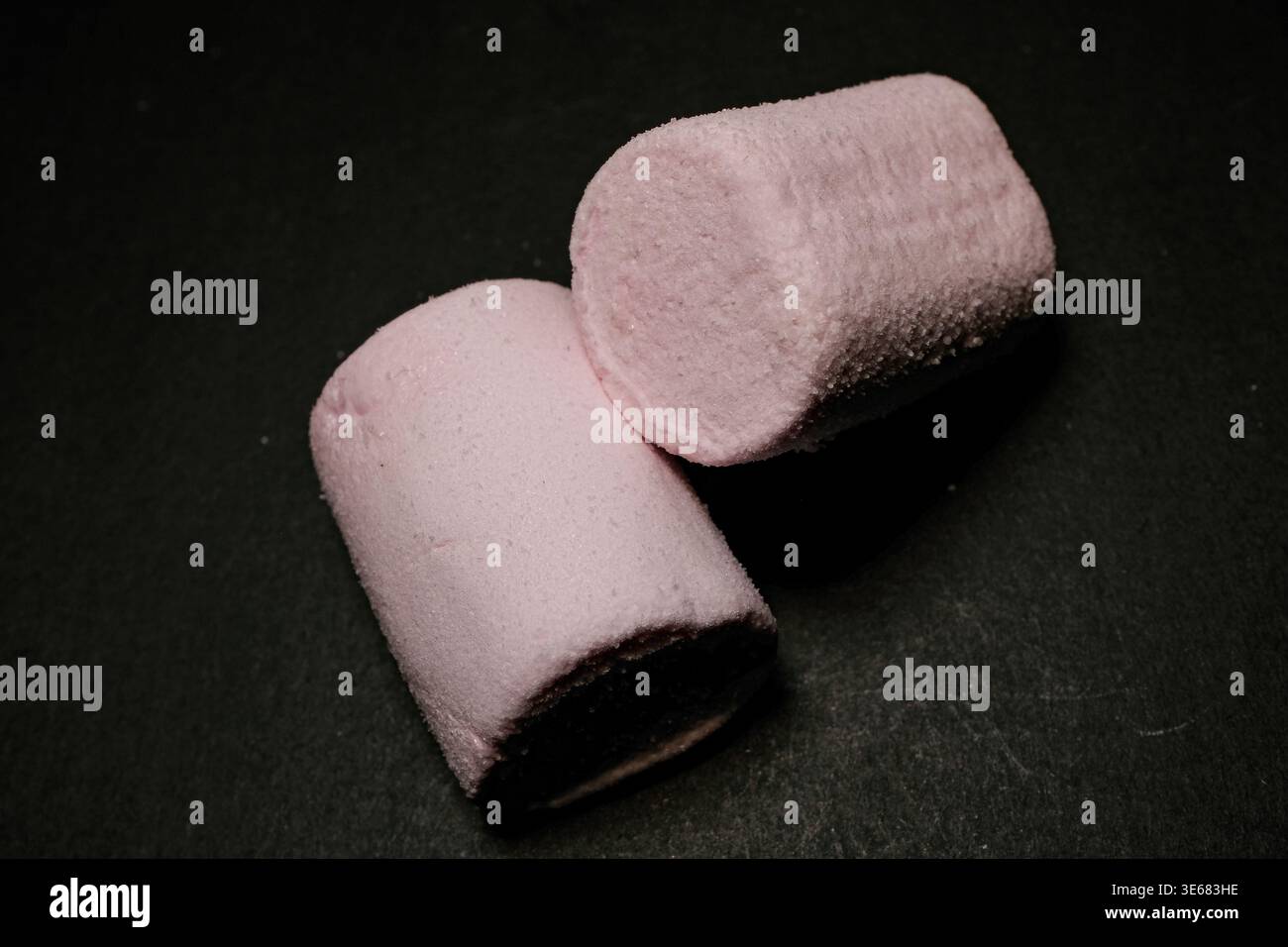 Two pink marshmallows on a dark surface, soft texture visible, studio-lit close-up Stock Photo