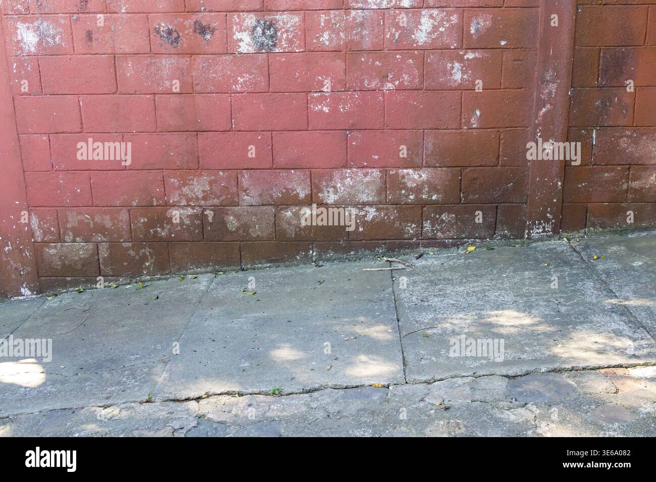 Weathered red brick wall with white spots on sidewalk Stock Photo