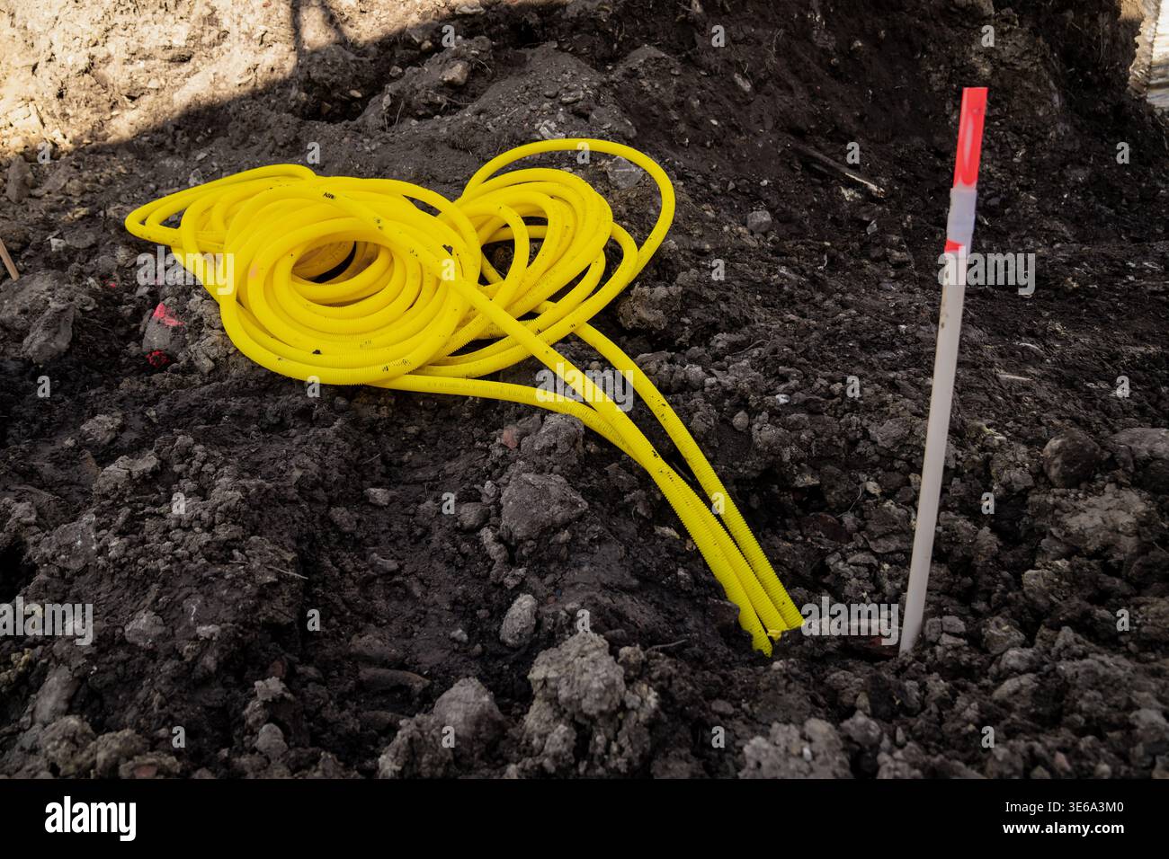 Coiled yellow corrugated conduit lying in dark earth near survey marker ...