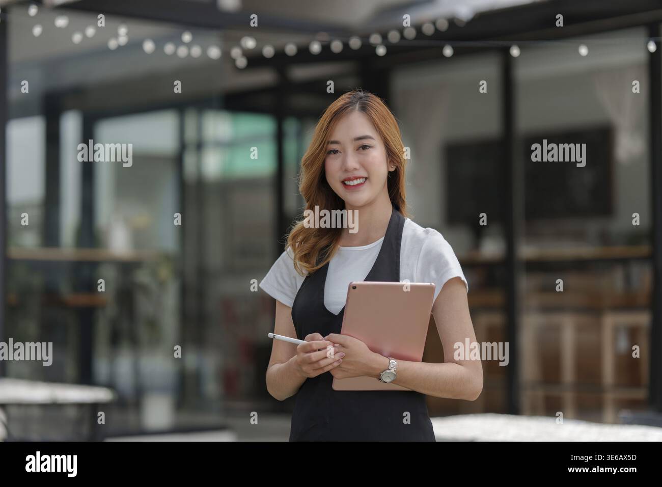 Beautiful Asian women Barista smiling and using tablet at her cafe Stock Photo