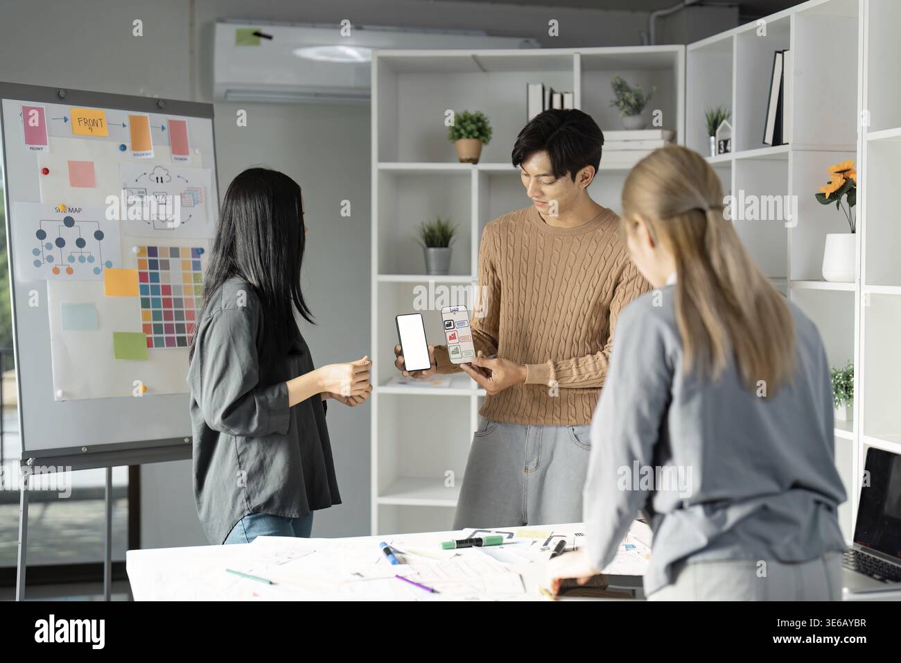 Designers showcasing a mobile app mockup during a UX UI presentation, emphasizing teamwork and interactive design processes in a creative workspace Stock Photo