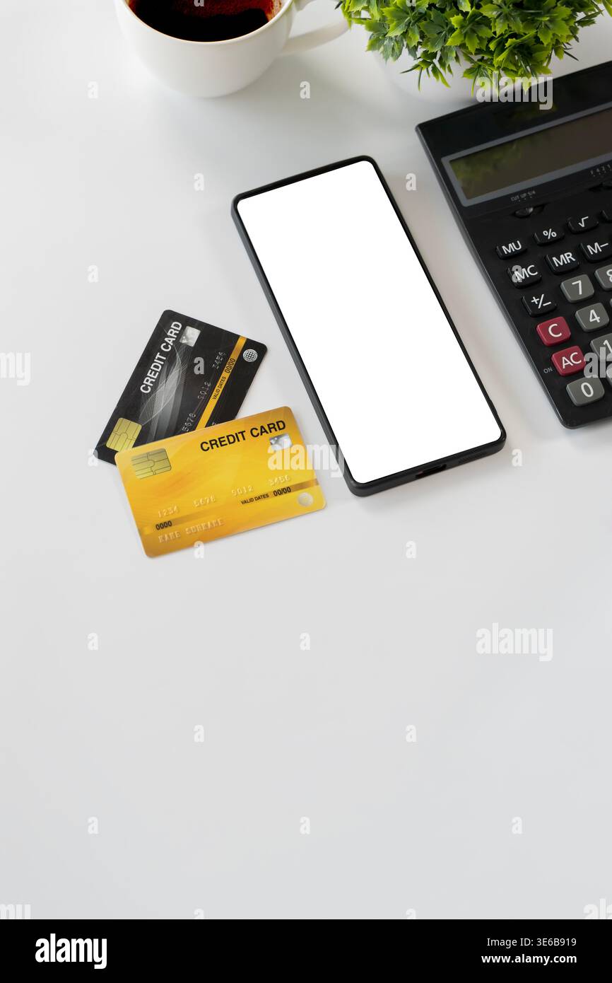 Flat lay of smartphone with blank screen, credit cards, calculator, coffee cup, and plant on white desk, ideal for mobile payment, ecommerce, banking, Stock Photo
