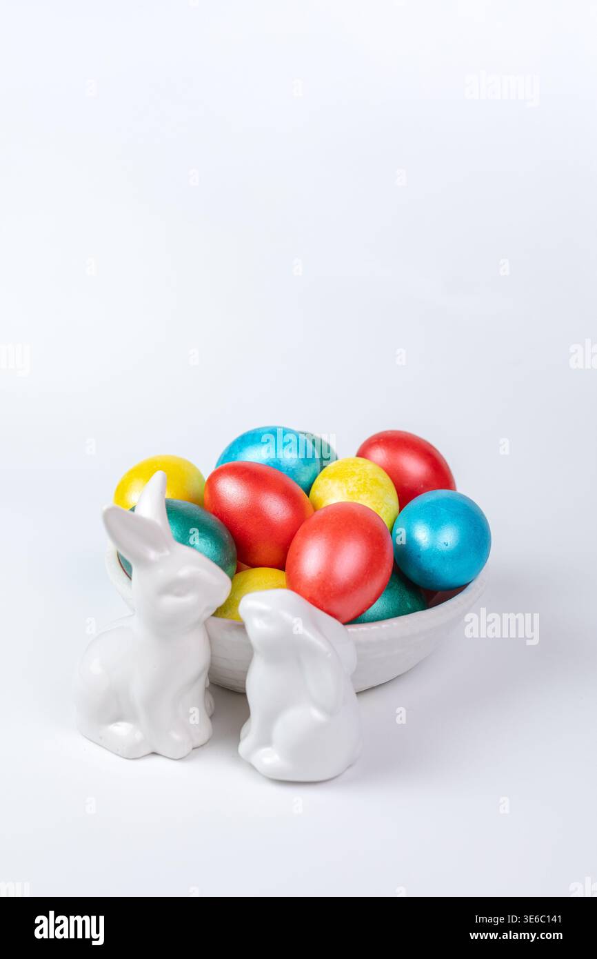 White Porcelain Bunnies and Painted Easter Eggs in Ceramic Bowl on White Background Stock Photo