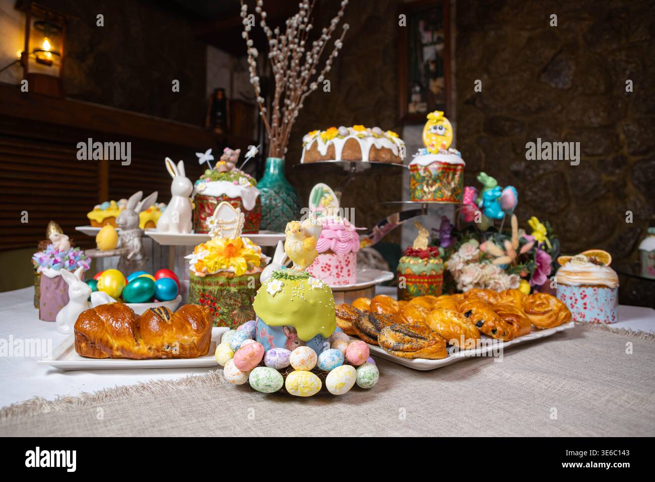 Festive Easter dessert table with colorful cakes, eggs, and floral decorations on stone wall Stock Photo