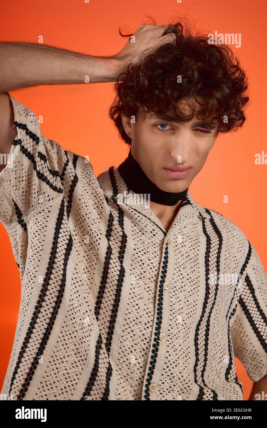 Curly haired man showcases his style in trendy clothes against an orange backdrop. Stock Photo