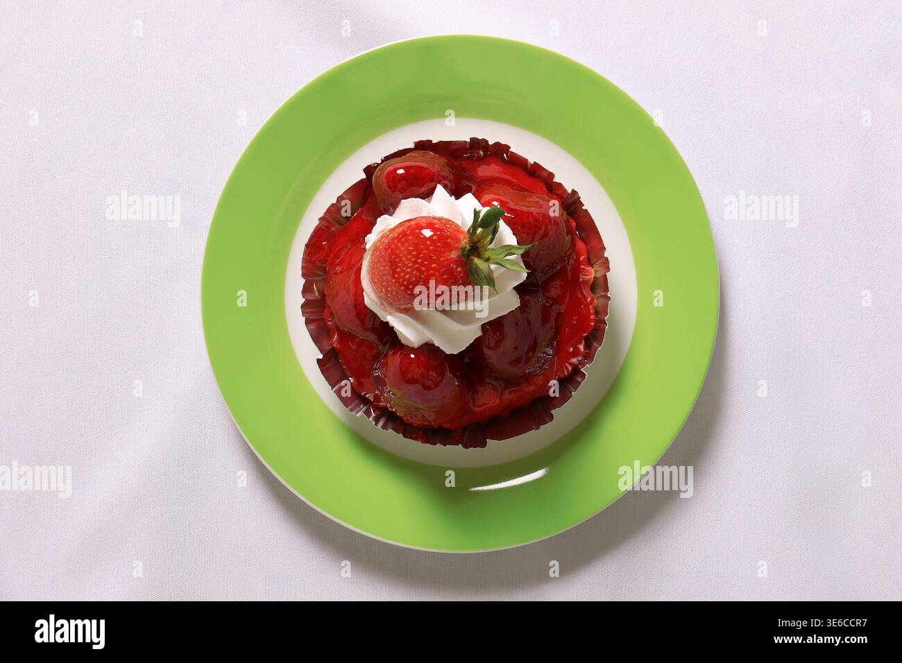 Small round strawberry tart topped with whipped cream served on a green and white plate over a white tablecloth. Stock Photo
