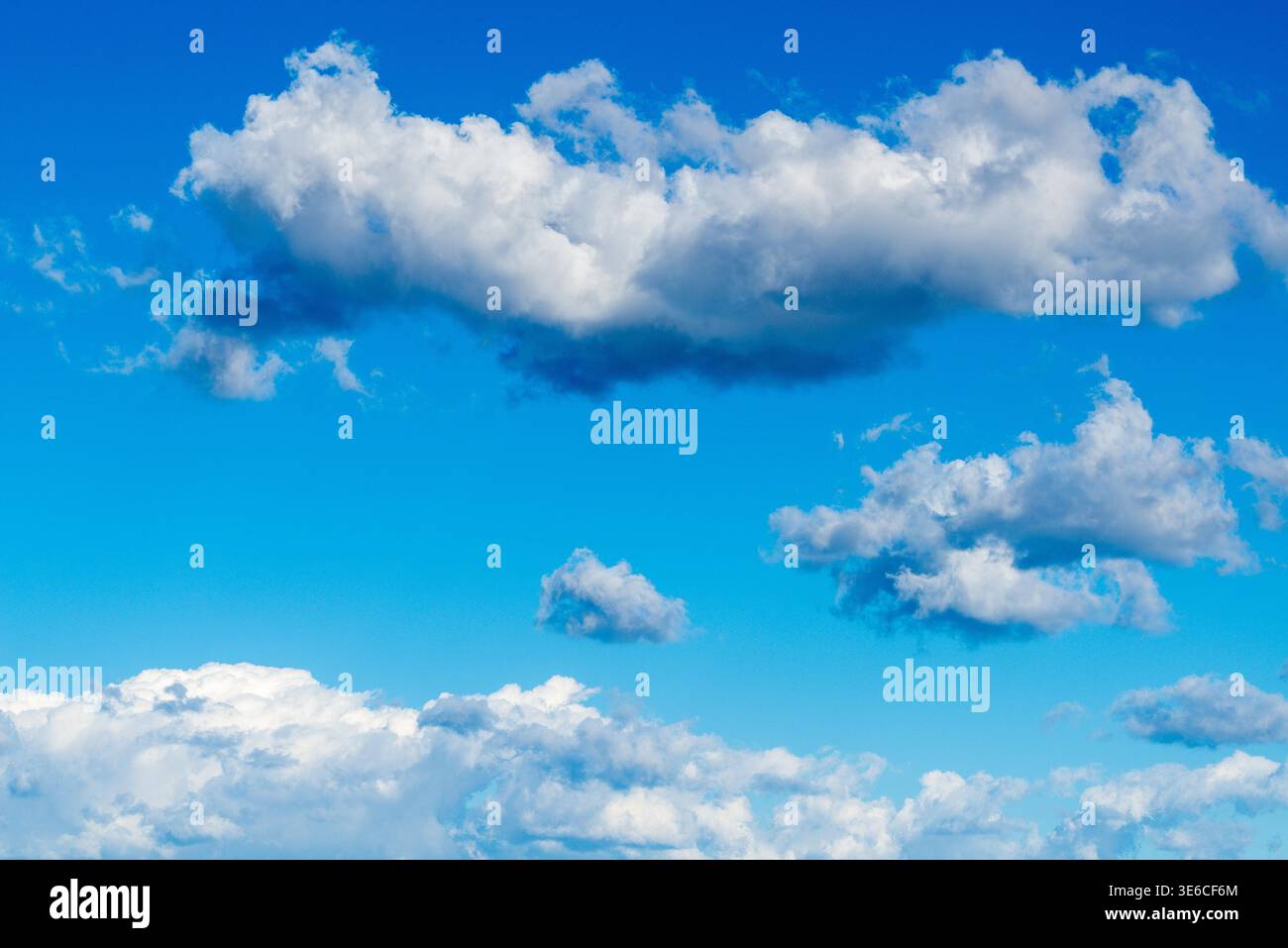 Bright blue sky is filled with soft cumulus cloud shapes, including a long dense cloud band and scattered smaller puffs in the distance. Stock Photo