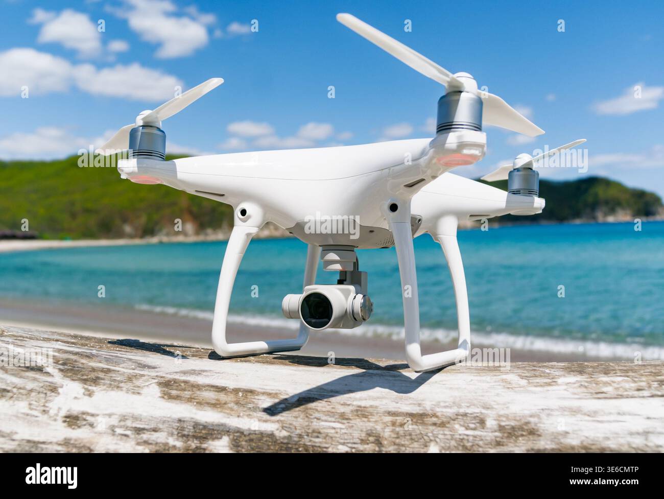 Modern white camera drone positioned on coastal surface overlooking beautiful blue ocean waters and green hills on a sunny day Stock Photo