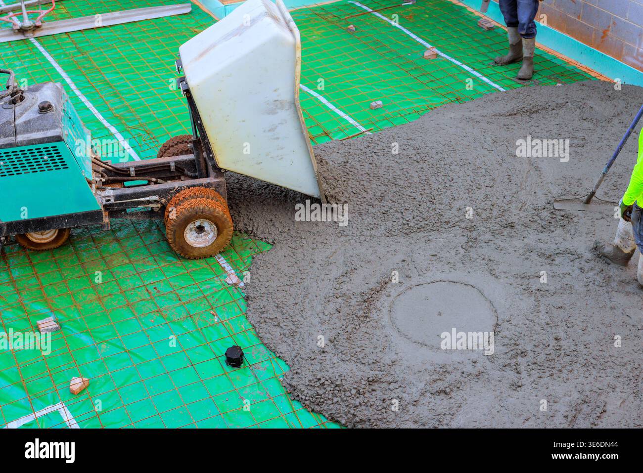 Two workers prepare spread concrete on construction site using wheelbarrow bucket Stock Photo