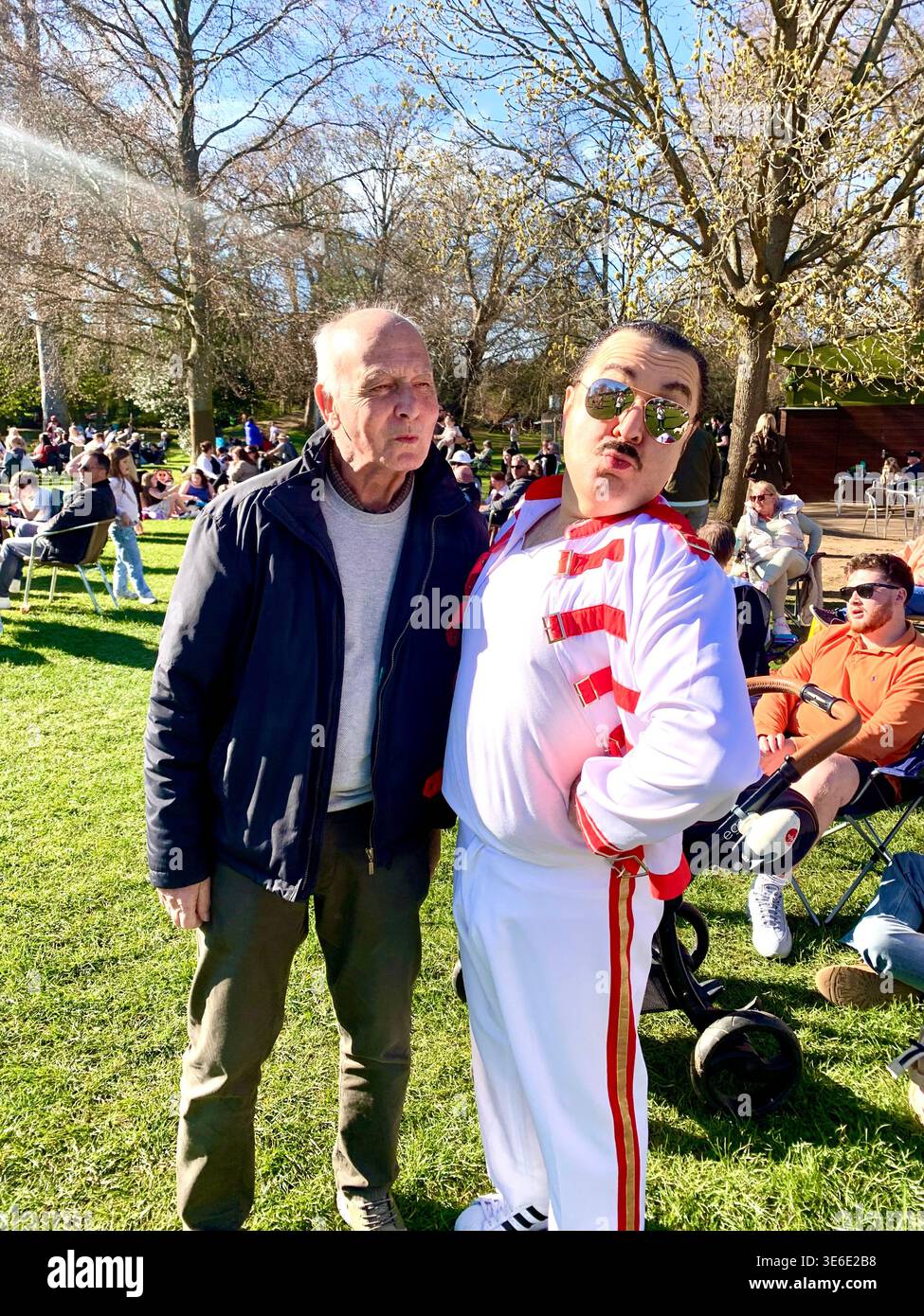 Freddie Mercury lookalike dressed in a white and red stage style costume poses in Abington Park Northampton near the bandstand confidently on a Sunday - Smartphone Captured Stock Image