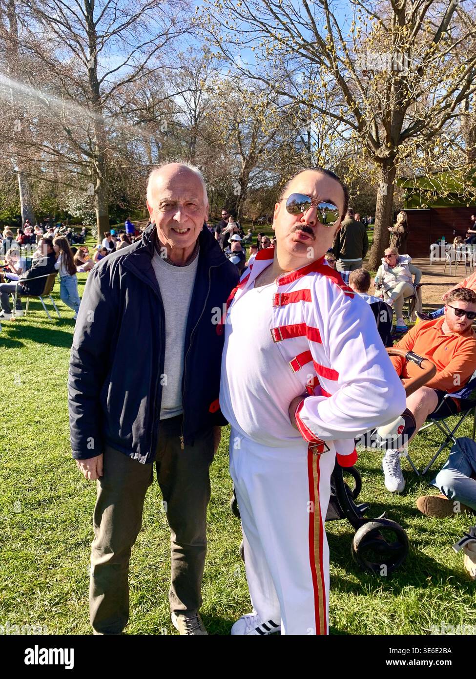 Freddie Mercury lookalike dressed in a white and red stage style costume poses in Abington Park Northampton near the bandstand confidently on a Sunday - Smartphone Captured Stock Image