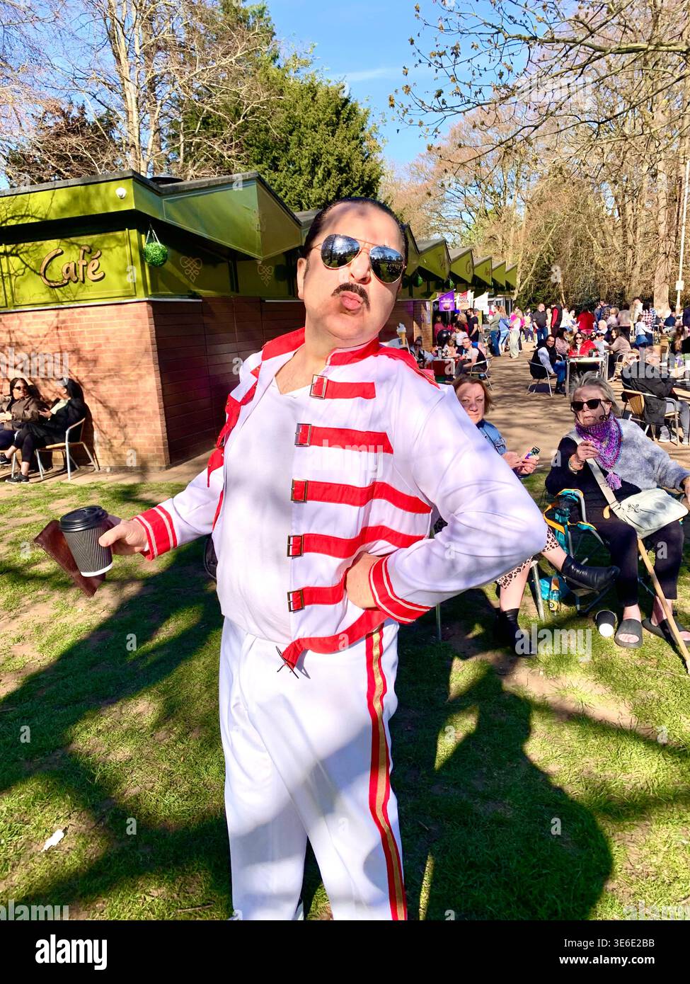 Freddie Mercury lookalike dressed in a white and red stage style costume poses in Abington Park Northampton near the bandstand confidently on a Sunday - Smartphone Captured Stock Image