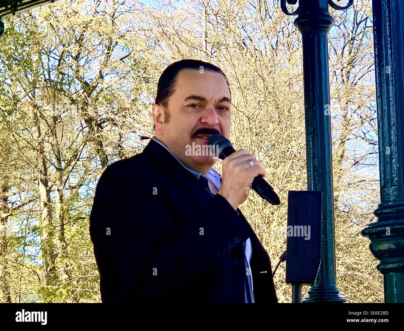 Freddie Mercury lookalike dressed in a white and red stage style costume poses in Abington Park Northampton near the bandstand confidently on a Sunday - Smartphone Captured Stock Image