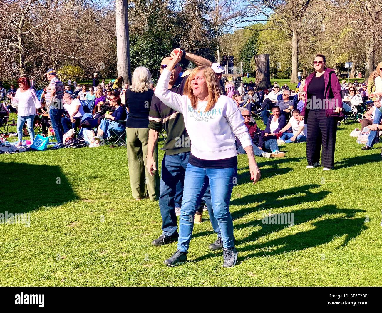 Freddie Mercury lookalike dressed in a white and red stage style costume poses in Abington Park Northampton near the bandstand confidently on a Sunday - Smartphone Captured Stock Image
