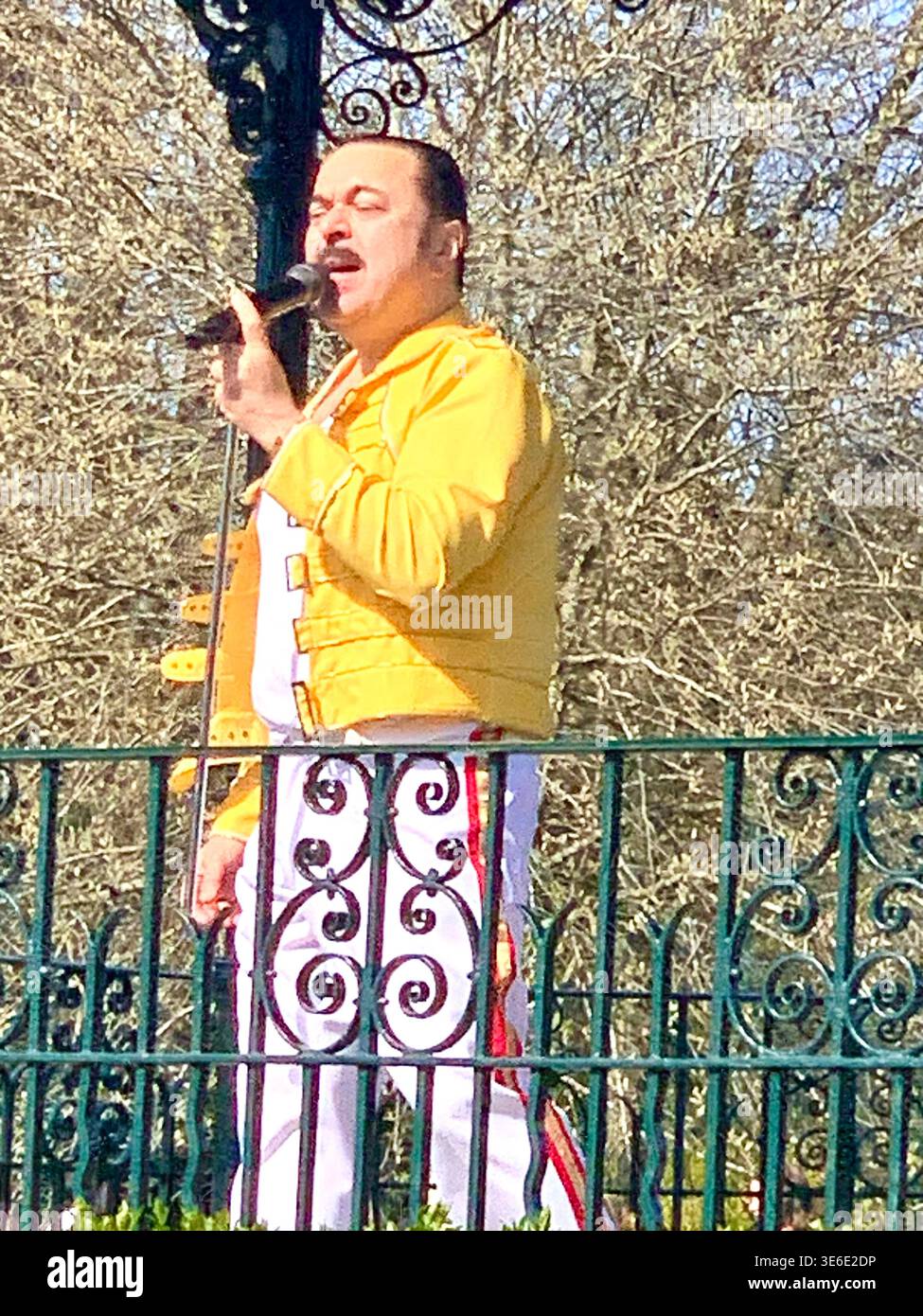 Freddie Mercury lookalike dressed in a white and red stage style costume poses in Abington Park Northampton near the bandstand confidently on a Sunday - Smartphone Captured Stock Image