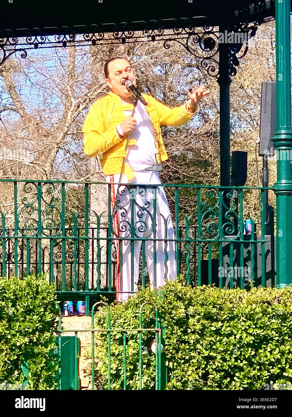 Freddie Mercury lookalike dressed in a white and red stage style costume poses in Abington Park Northampton near the bandstand confidently on a Sunday - Smartphone Captured Stock Image