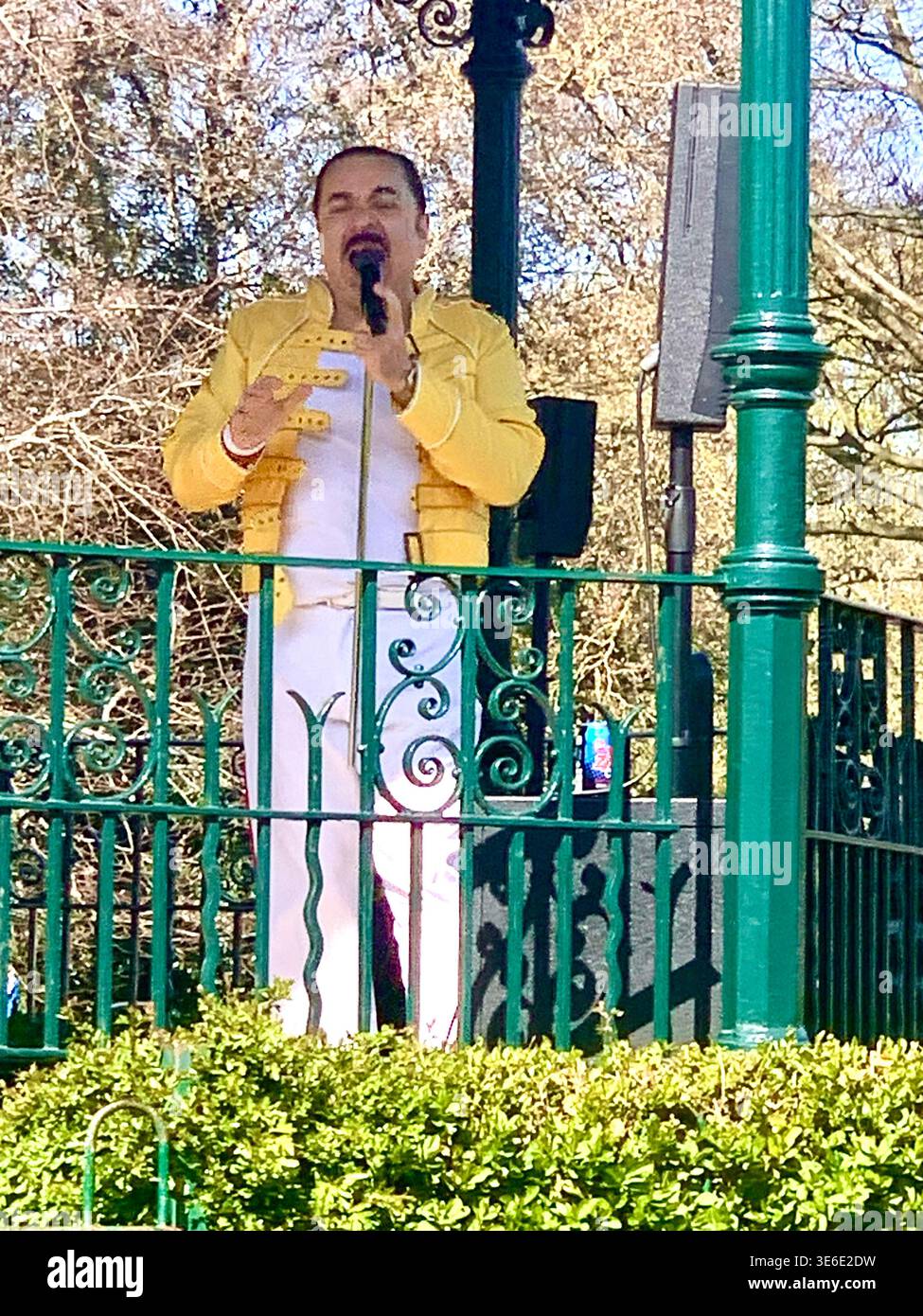 Freddie Mercury lookalike dressed in a white and red stage style costume poses in Abington Park Northampton near the bandstand confidently on a Sunday - Smartphone Captured Stock Image