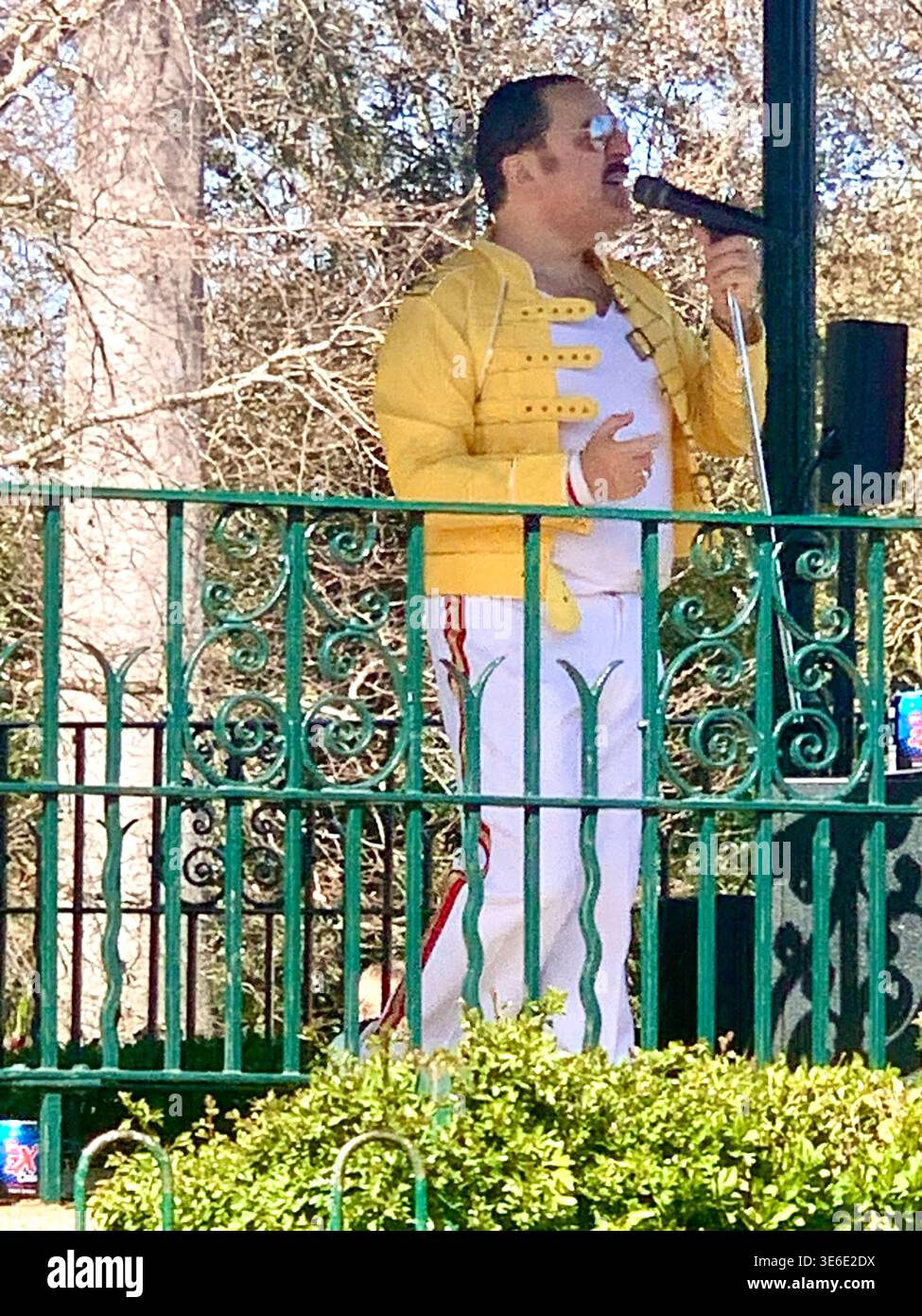 Freddie Mercury lookalike dressed in a white and red stage style costume poses in Abington Park Northampton near the bandstand confidently on a Sunday - Smartphone Captured Stock Image
