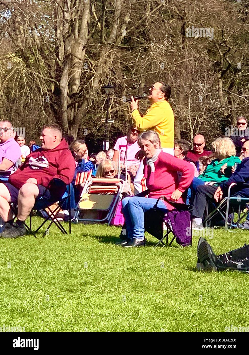 Freddie Mercury lookalike dressed in a white and red stage style costume poses in Abington Park Northampton near the bandstand confidently on a Sunday - Smartphone Captured Stock Image
