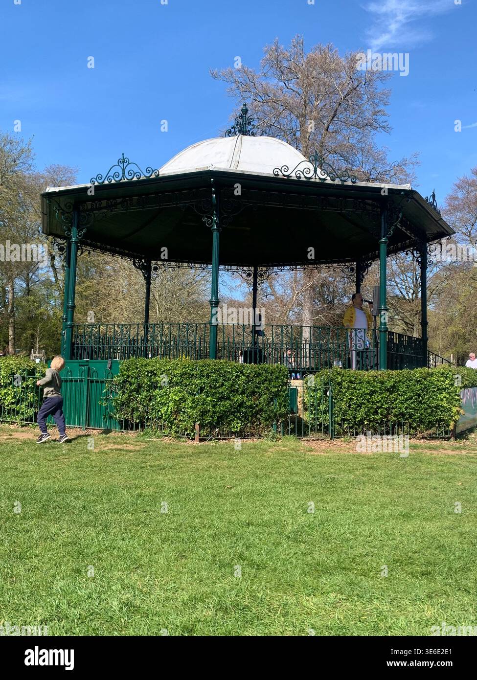 Freddie Mercury lookalike dressed in a white and red stage style costume poses in Abington Park Northampton near the bandstand confidently on a Sunday - Smartphone Captured Stock Image