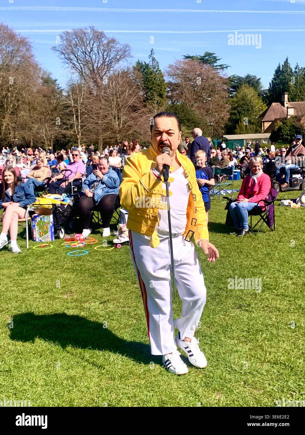 Freddie Mercury lookalike dressed in a white and red stage style costume poses in Abington Park Northampton near the bandstand confidently on a Sunday - Smartphone Captured Stock Image