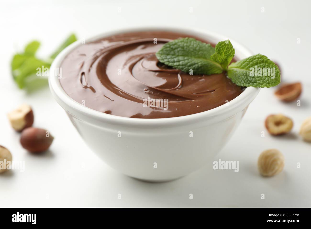 Tasty chocolate paste and hazelnuts on white table, closeup Stock Photo