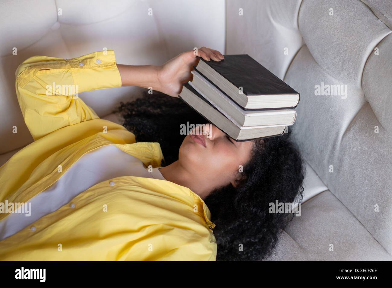 Brunette woman lying on the sofa and feeling tired after studying Stock Photo