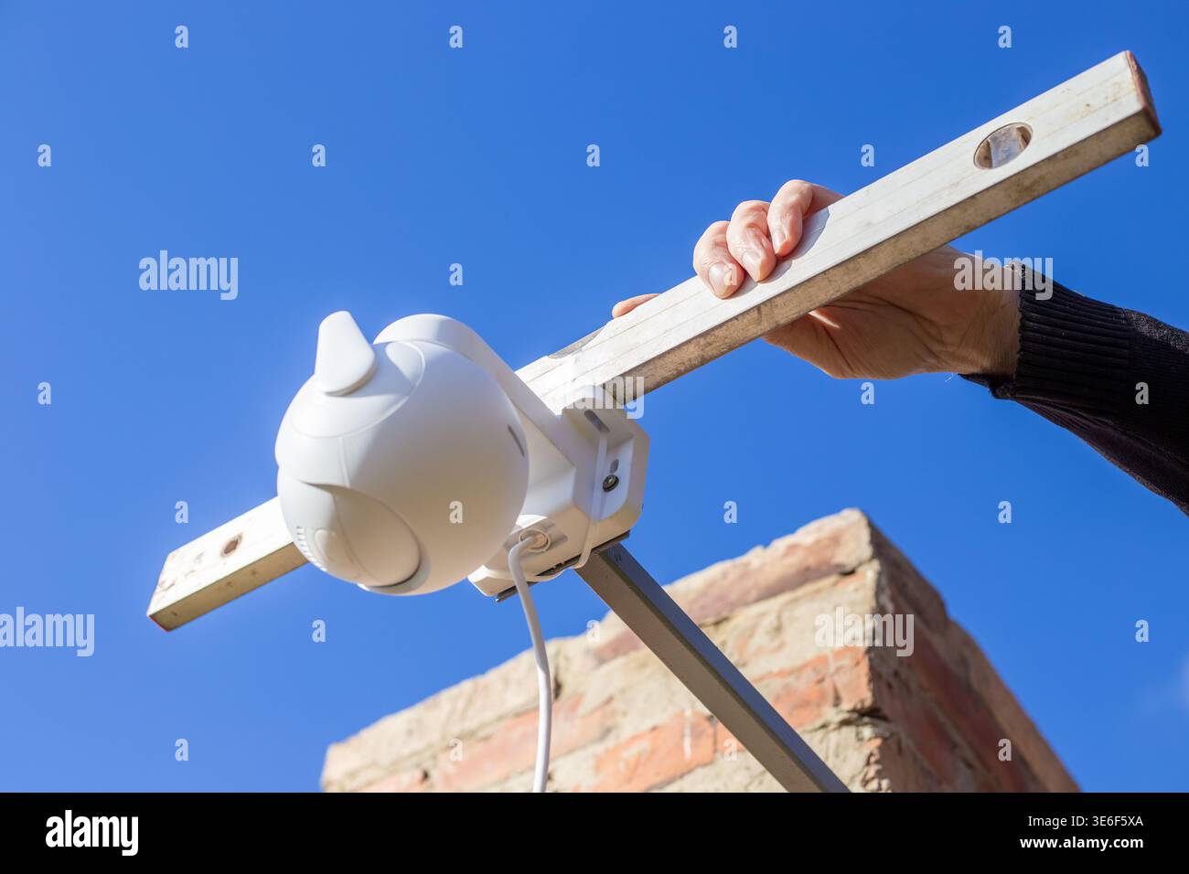 Hands checking the level of a white plastic CCTV camera mounted on a metal bracket. Security system, precise installation, technology setup. Stock Photo