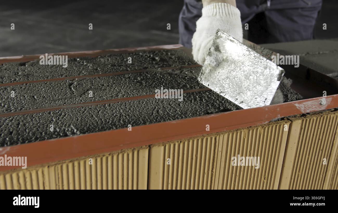 Construction worker using trowel for levelling raw mortar for the brick layers fixation. Close up of cement being put on red bricks Stock Photo