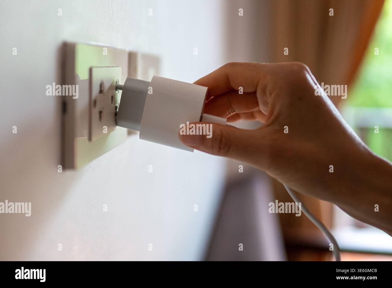 Woman hand holding mobile charger plugging in outlet on wall in room ...