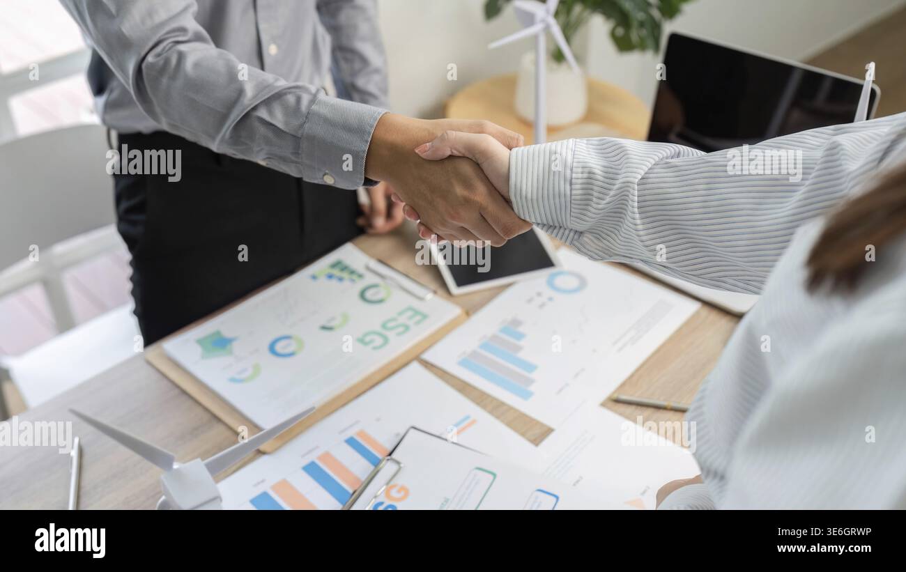 Two professionals shaking hands over ESG documents, representing a commitment to sustainable business practices Stock Photo
